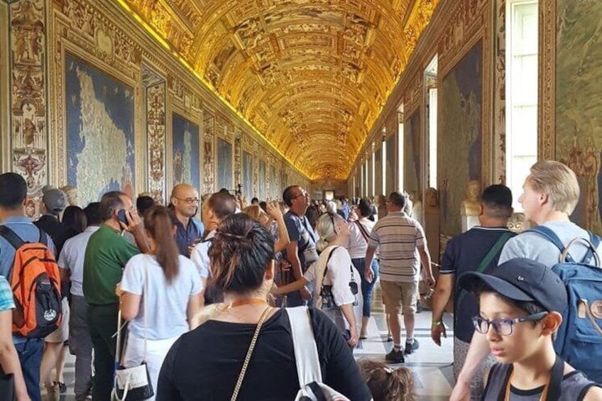 A crowded corridor with ornate golden ceilings and classical artwork. 3