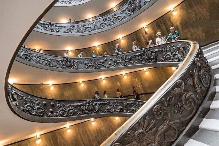 A spiral staircase with ornate metal railings and people ascending and descending. 1