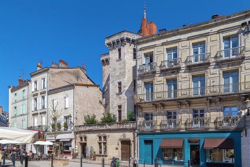 A historic European town square with a prominent tower, traditional buildings, and a café. 3