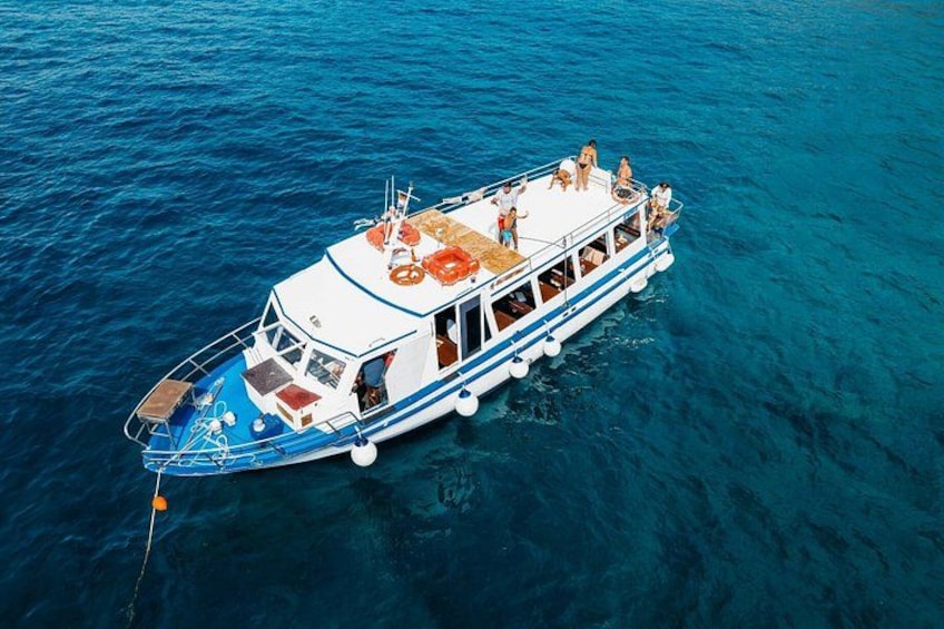 A boat with people on deck, floating on clear blue water. 2