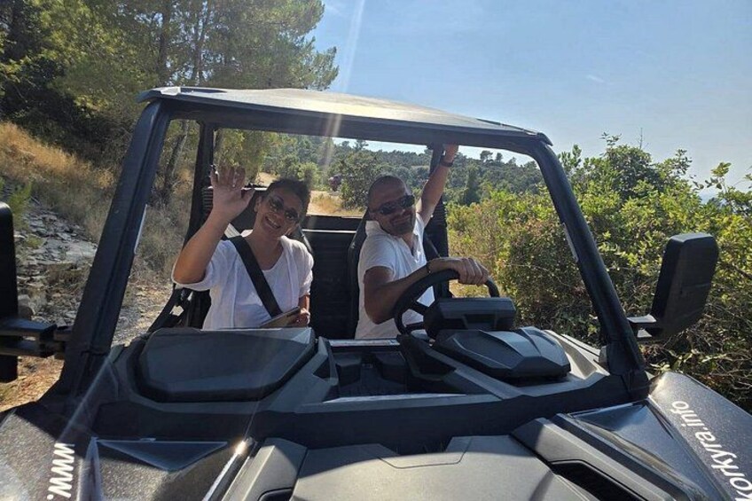 Two people in a vehicle with a sunroof, surrounded by greenery and a clear sky. 2