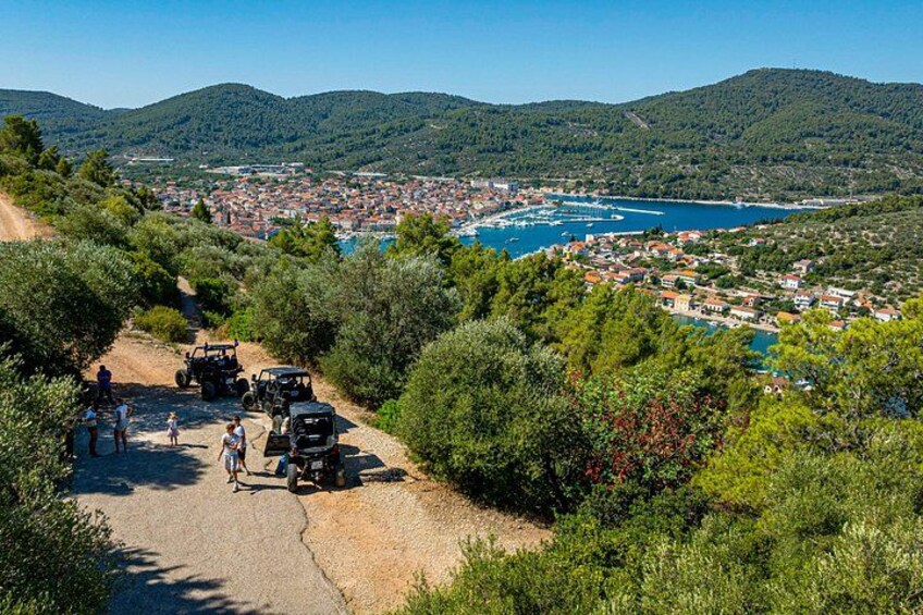 A coastal town with a dirt road, parked vehicles, and people walking. 1