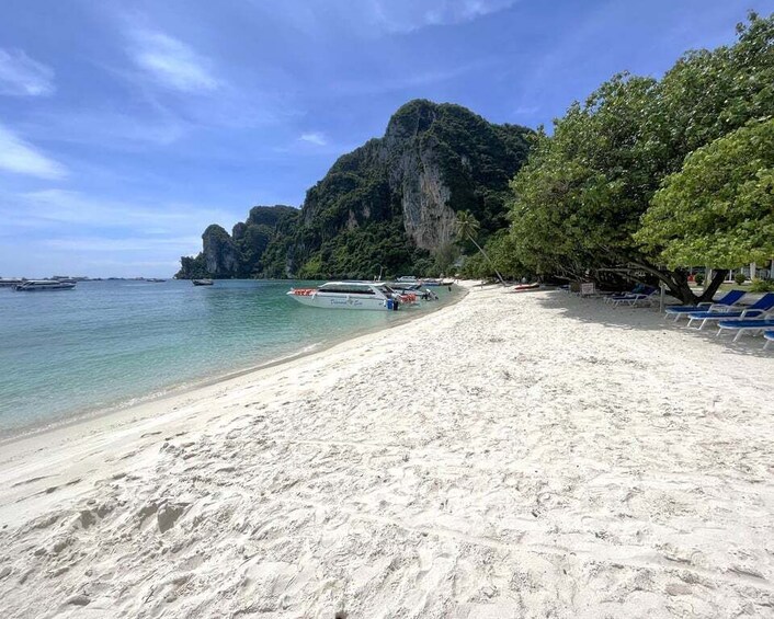 A beach with white sand, clear turquoise water, boats, and a large mountain in the background. 4