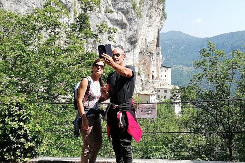 Two people taking a selfie with a scenic mountain backdrop and a church. 1