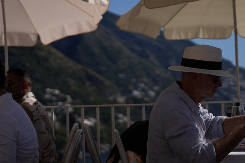 A person wearing a hat and a white shirt sitting at a table with a mountain in the background. 3