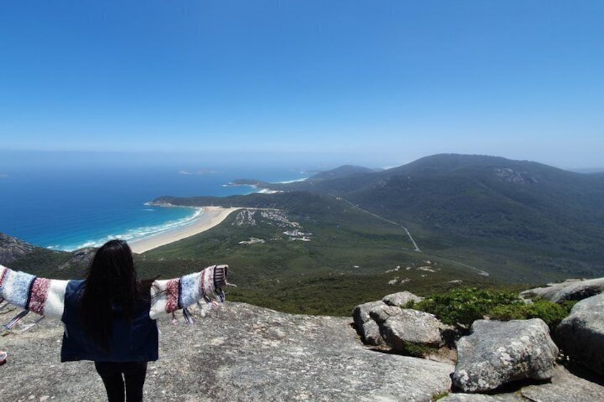 A person standing on a rocky outcrop overlooking a beach and mountains. 1