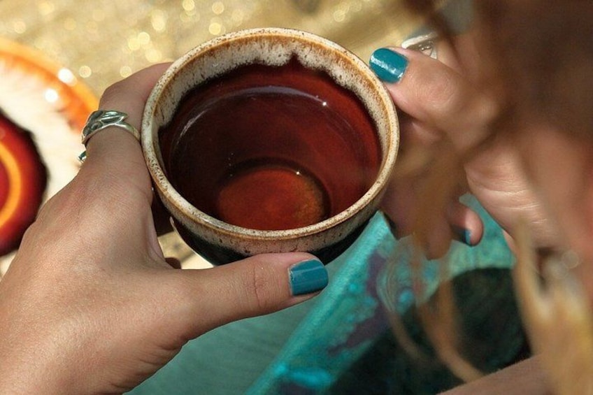 A person holding a ceramic mug with a brown liquid, wearing a turquoise ring, and a turquoise nail polish. 4