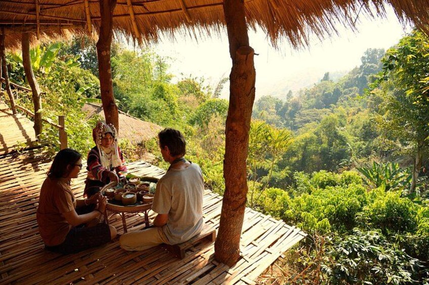 A group of people sitting at a wooden table under a thatched roof, surrounded by lush greenery. 4