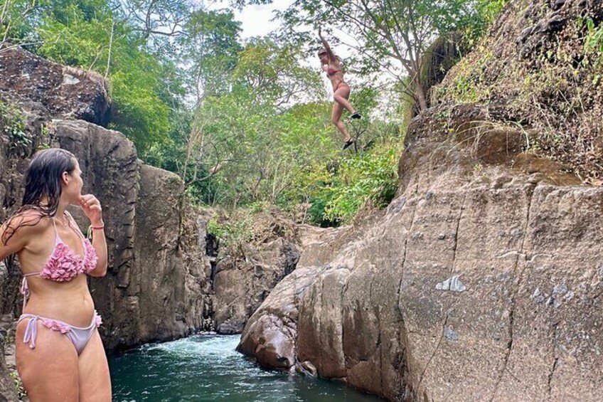 A rocky landscape with a river, a person in a bikini, and another person jumping. 2