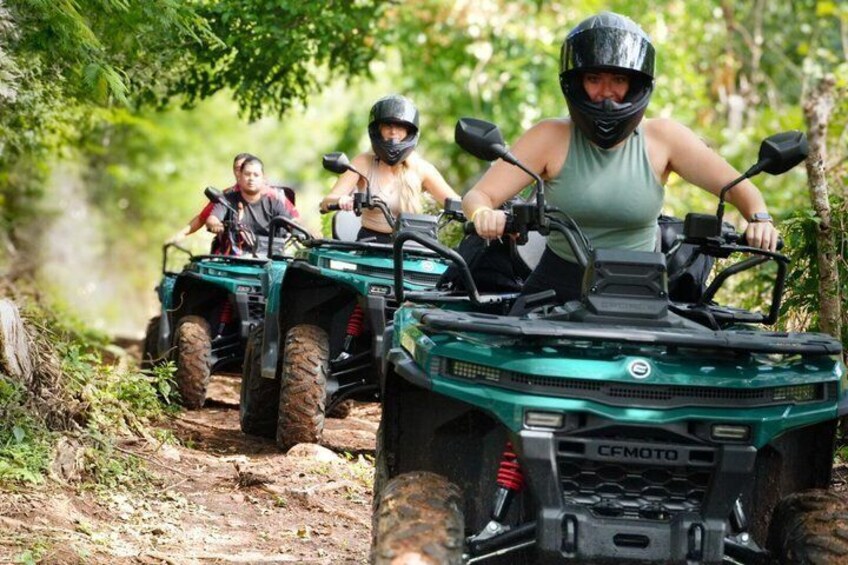 Two people riding ATVs on a dirt path surrounded by greenery. 1