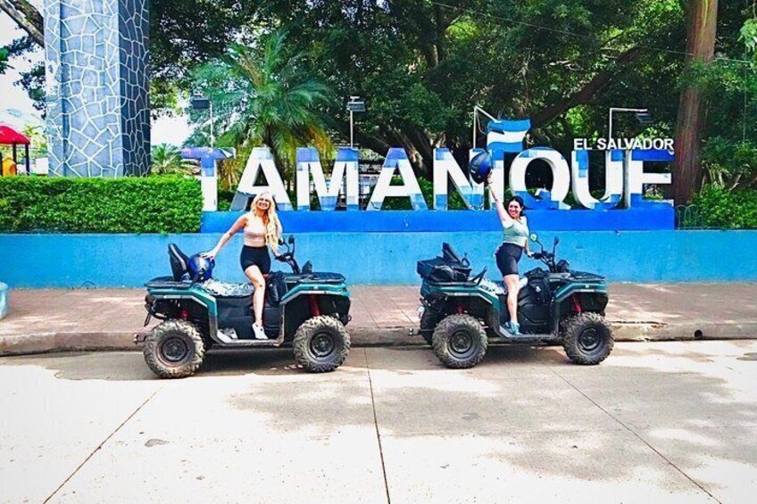 Two people on ATVs in front of a sign that reads 'TAMANQUE'. 5