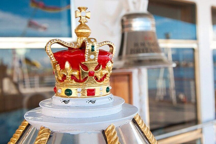 A decorative golden crown with jewels on a clear glass base. 3