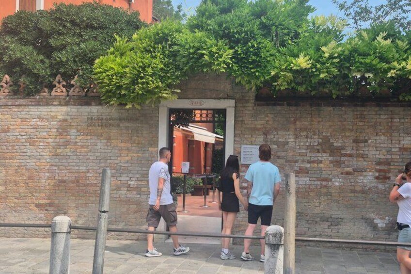 A brick wall with a gate, greenery above, and people standing in front. 5
