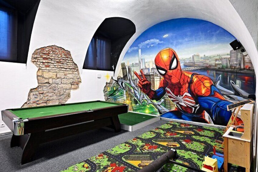 A pool table with a green felt surface, a Spiderman mural on the wall, and a stone sculpture. 1