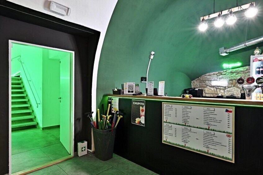 A green interior with a reception desk, a menu board, and a staircase leading to a bright green area. 3