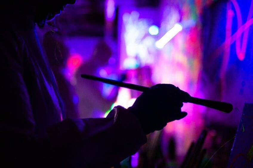 A person holding a stick, possibly a walking stick, in a dimly lit environment with colorful lights in the background. 3