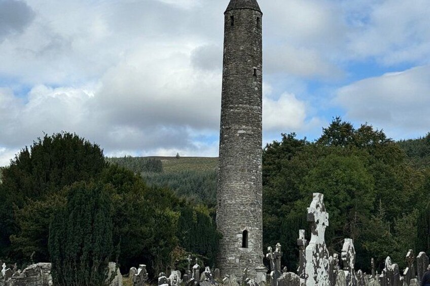 A tall, narrow tower with a pointed top, surrounded by trees and a cemetery with headstones. 5