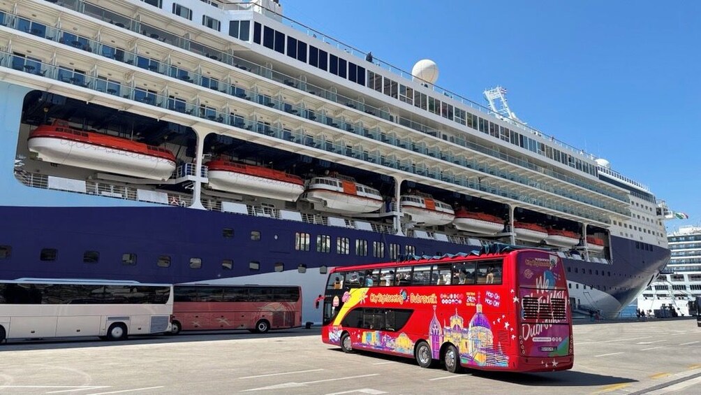 Et stort krydstogtskib ligger ved kaj, med en rød turistbus med to etager foran. 5