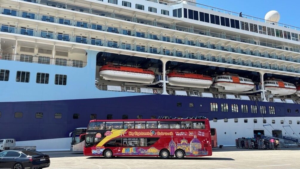 Et stort krydstogtskib med flere dæk og en rød turistbus foran. 4