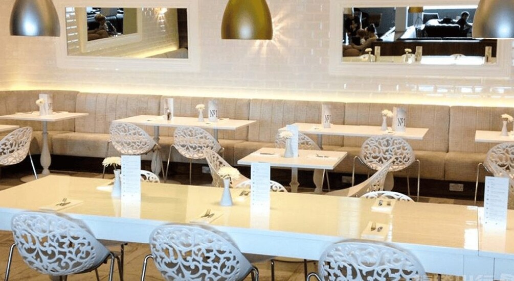 A modern restaurant interior with white furniture, including tables and chairs, and a beige-colored sofa area. 2