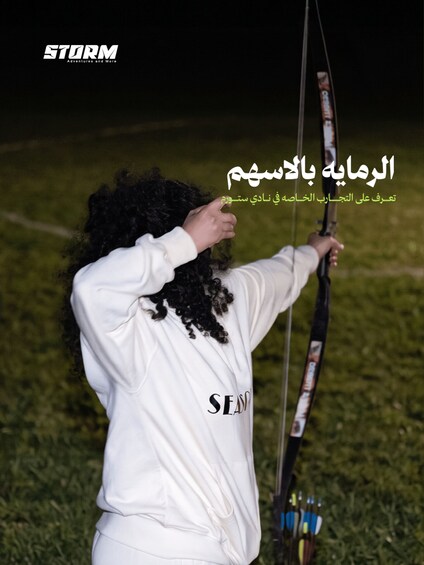 A person in a white sweatshirt aiming a bow and arrow. 5