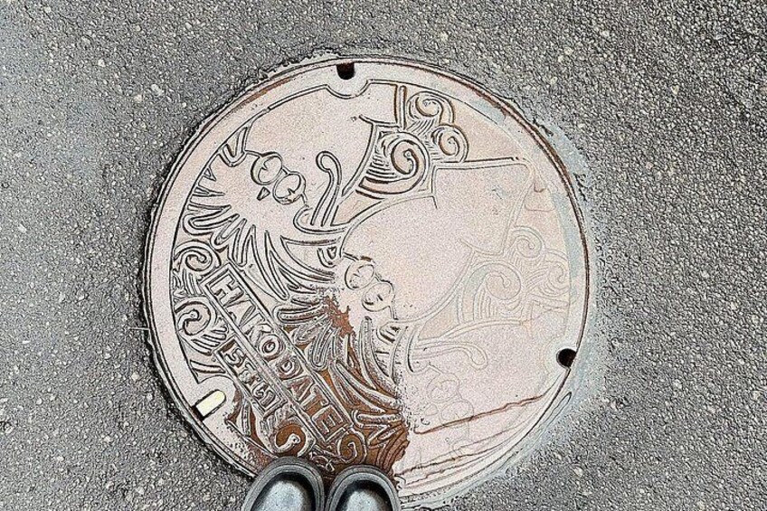 A manhole cover with intricate designs and a pair of shoes at the bottom. 5
