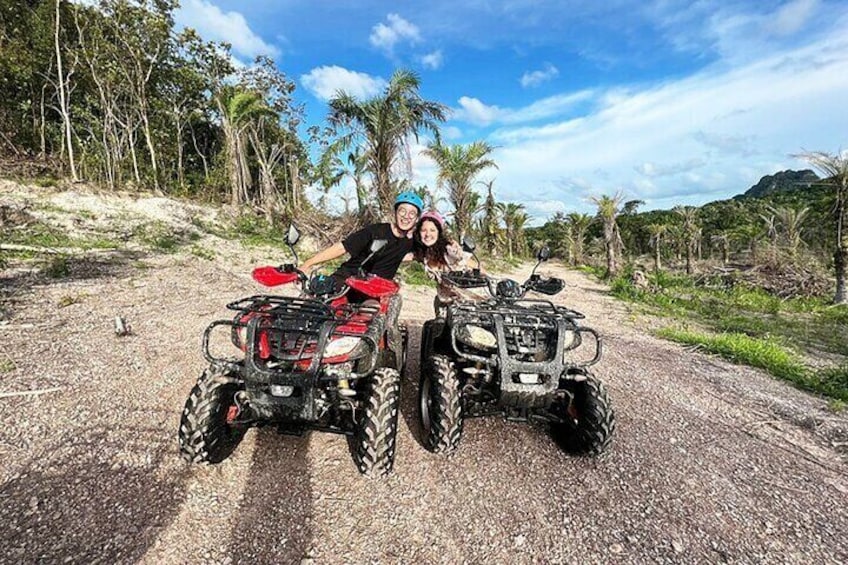 Two ATVs on a dirt road with palm trees and a mountain in the background. 2