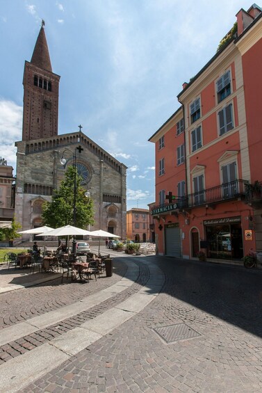 A cobblestone square with outdoor seating, a church with a bell tower, and a building with a pharmacy. 5