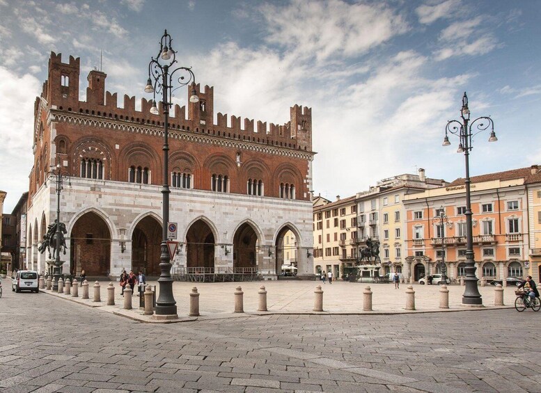A historic building with arched windows and a tower, surrounded by cobblestone pavement and classic street lamps. 1