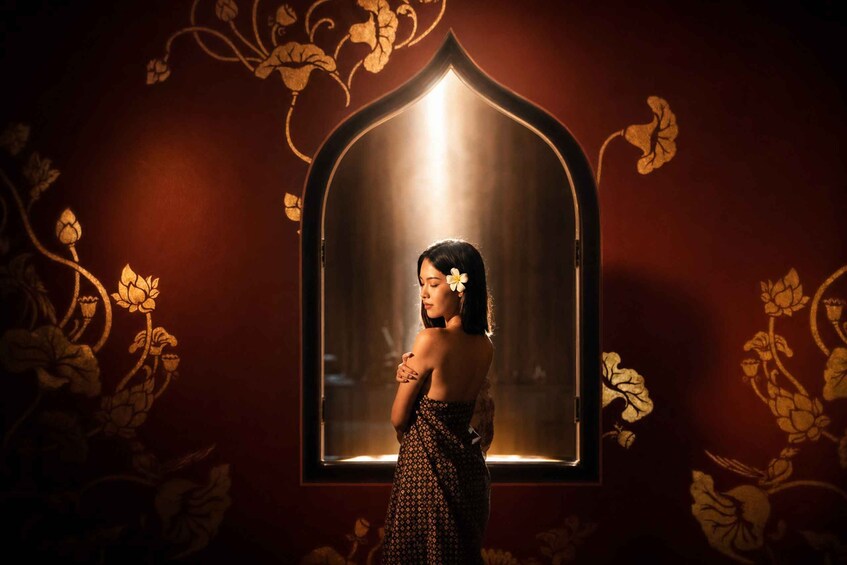 A person standing in front of a decorative mirror with floral patterns on the wall. 3