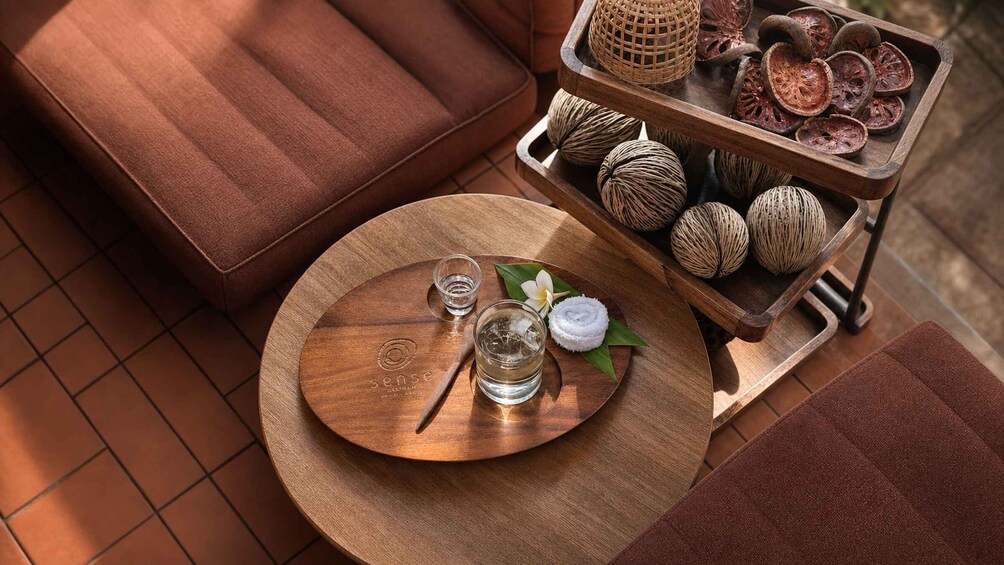 A wooden table with a tray, a glass of water, a white flower, and a woven basket with dried plant slices. 2