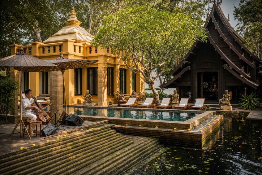 A pool with lounge chairs, a statue, and traditional architecture. 4