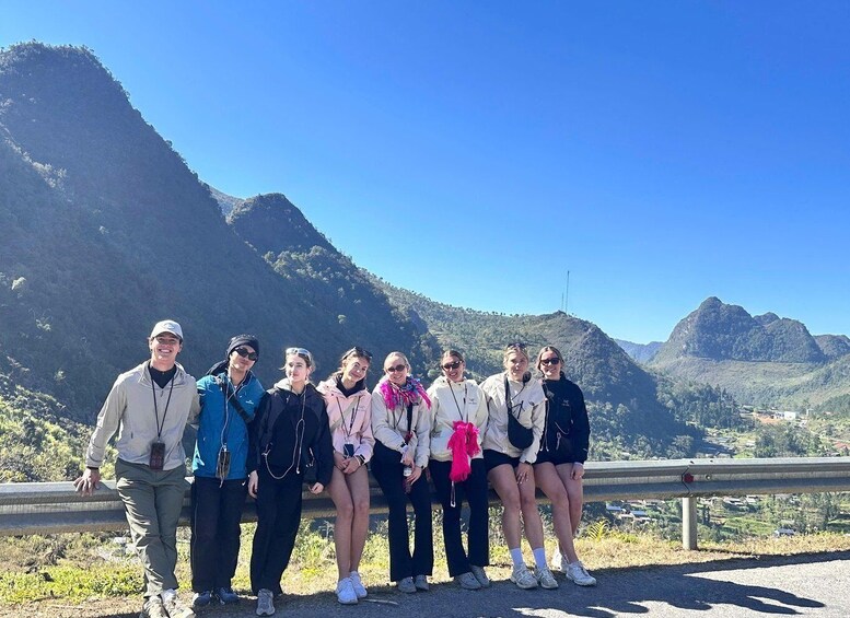 A group of people standing on a roadside with a mountainous landscape in the background. 2