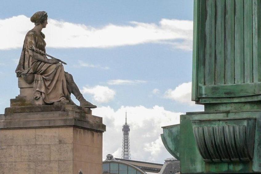 A statue of a seated woman on a pedestal, a green structure, and a tower in the background. 1