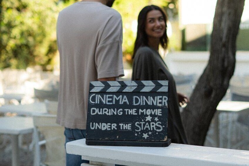 A clapperboard with text 'CINEMA DINNER DURING THE MOVIE UNDER THE STARS' on a white surface. 4