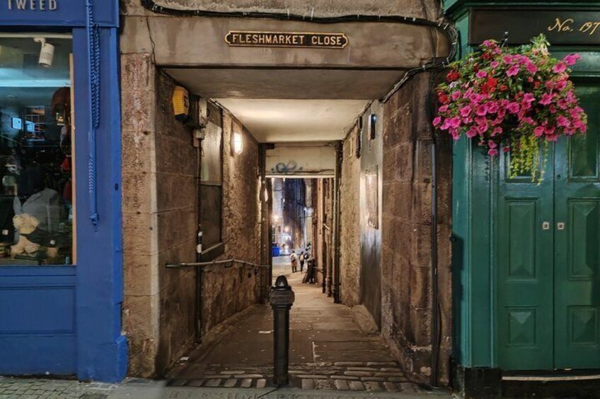 A narrow alleyway with a 'FLESHMARKET CLOSE' sign, a blue shop on the left, and a green door with a flower basket on the right. 3