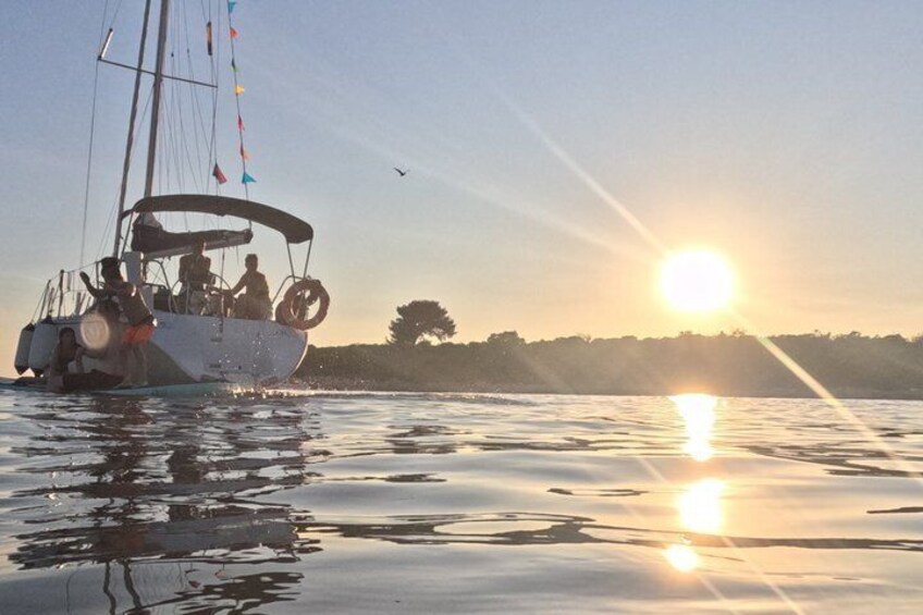 A sailboat on calm water with the sun setting in the background. 2