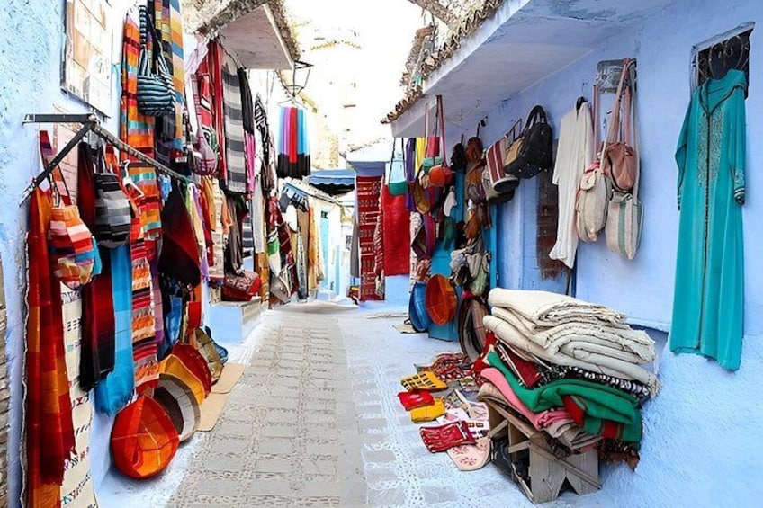 A narrow street with colorful textiles and bags displayed on the walls. 3