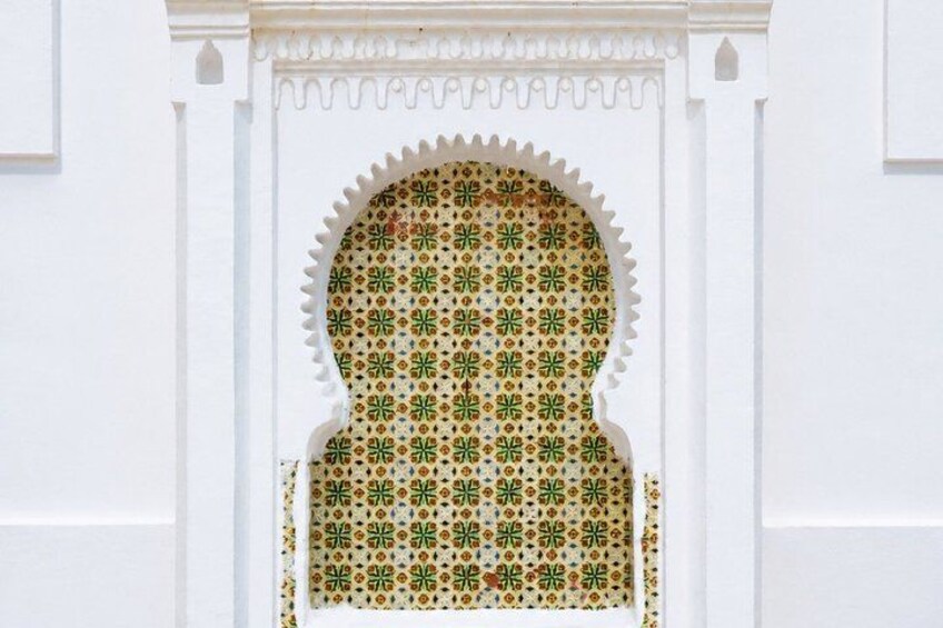 A white wall with a decorative archway featuring intricate tile patterns. 2