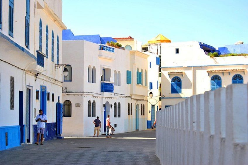 A narrow street with white buildings and blue doors and windows. 2