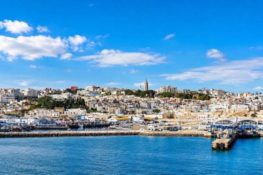 A coastal cityscape with a prominent tower, a marina with boats, and a clear blue sky. 2