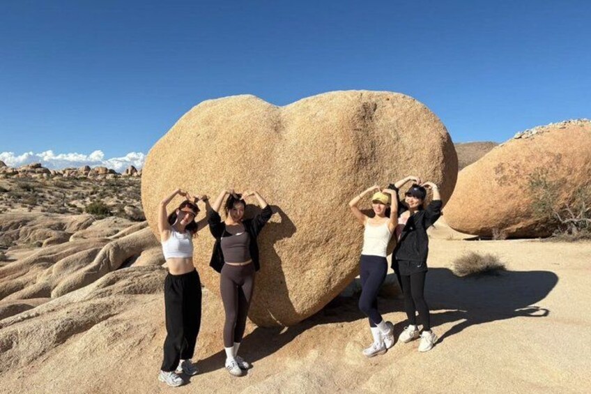 Four people posing in front of a large rock formation in a desert landscape. 2