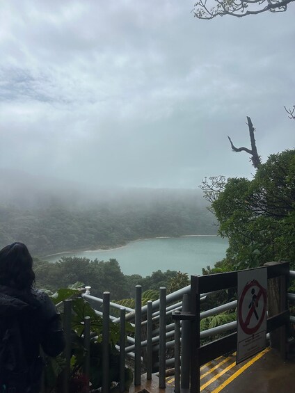 A foggy landscape with a body of water, a forested area, and a railing with a no-entry sign. 3