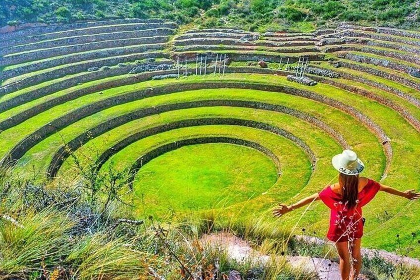 A person in a red dress and white hat standing on a path with arms outstretched, overlooking terraced agricultural fields. 2