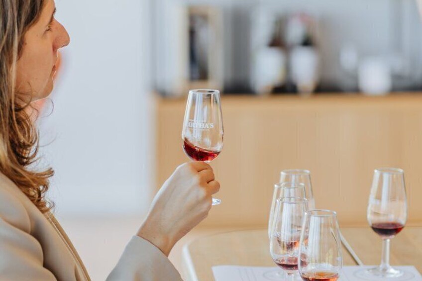 A person holding a wine glass with red wine, seated at a table with several empty wine glasses. 1