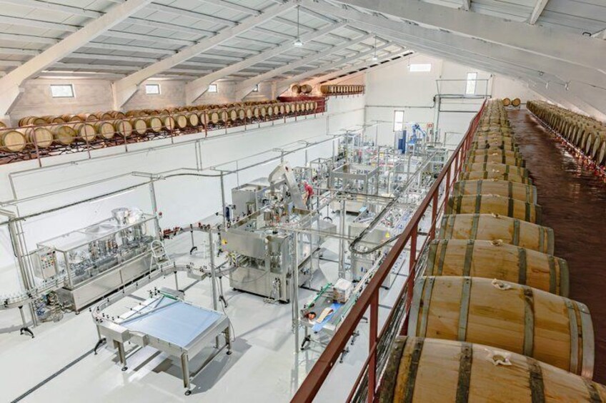A large industrial facility with rows of wooden barrels and stainless steel processing equipment. 4