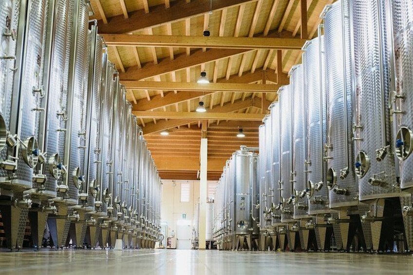 A large industrial facility with rows of stainless steel tanks and wooden beams on the ceiling. 1
