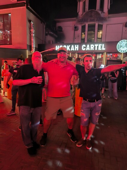 Three people walking on a brick pavement with a building in the background displaying a sign that reads 'HOOKAH CARTEL'. 2