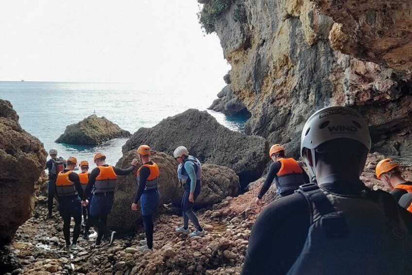 A group of people wearing helmets and life vests on a rocky coastal area. 4