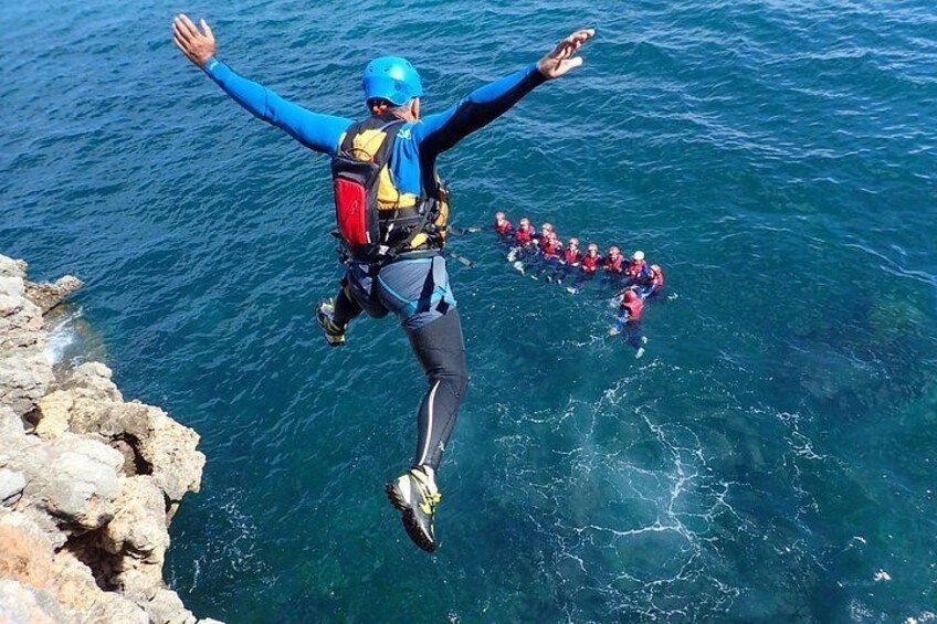 A person jumping off a cliff into the ocean with a group of people below. 1